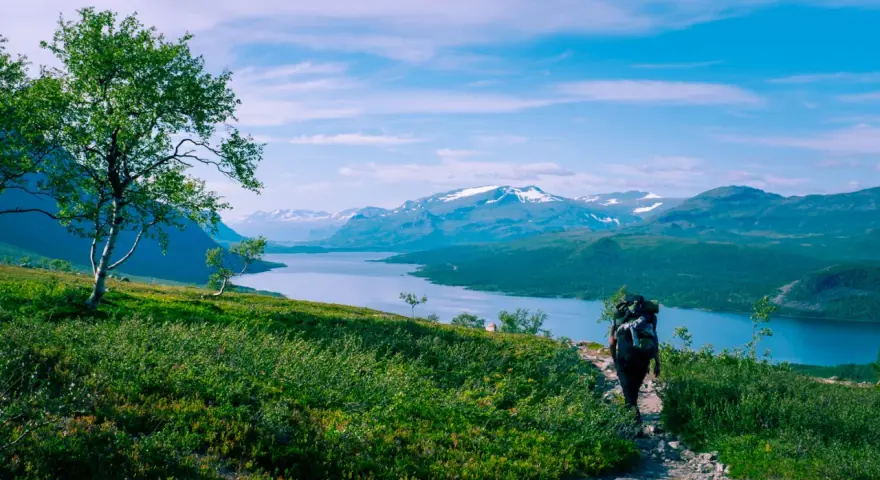 Vandrare med stor ryggsäck på en stenstig, njuter av storslagna vyer över sjö och snöklädda berg. Perfekt för vandringsleder Norrland.