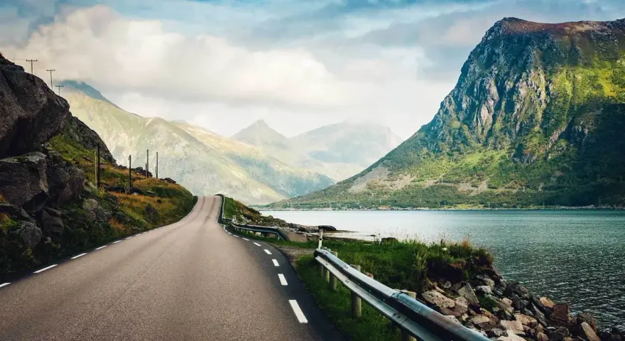 Väg som slingrar sig genom dramatiskt landskap med berg och fjord. En drömresa till Lofoten från Stockholm.