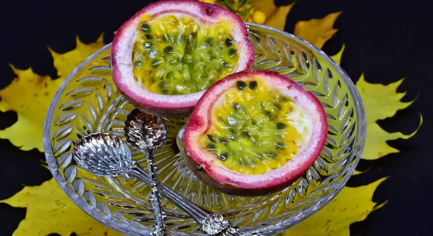 Två halvor av passionsfrukt på en kristallskål, omgivna av höstlöv. Dessa exotiska frukter ser läckra ut!