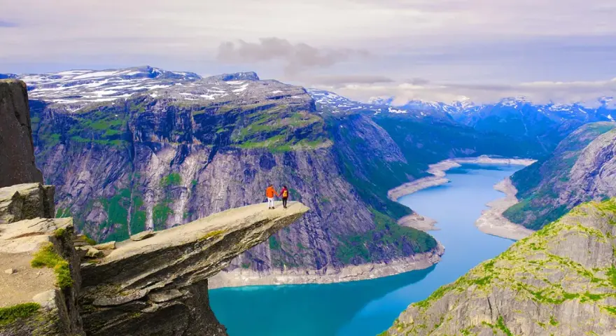 Två personer står på Trolltunga, en klippavsats i Norge, med en fantastisk utsikt över bergen och naturen.