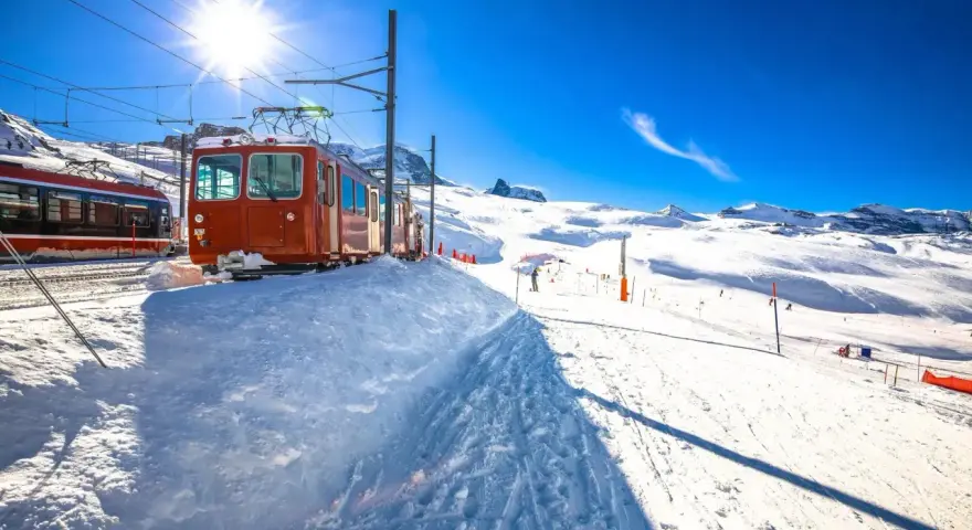 Ett snötäckt tåg i Schweiz, redo att transportera skidåkare uppför berget under en strålande solig dag.