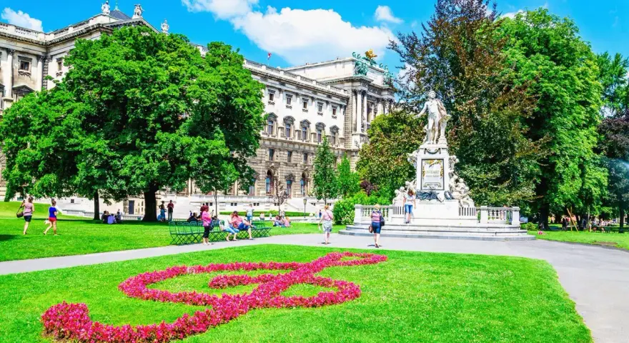 En vacker sommardag i Wien. En blomsterformation i form av en fiolnyckel lyser upp gräsmattan framför Mozarts staty. Ett perfekt ställe att se i Wien.