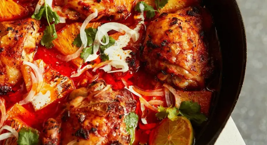 Saftiga kycklinglår i en kryddig röd sås med apelsinsegment, lök och koriander. En smak av brasilien mat.