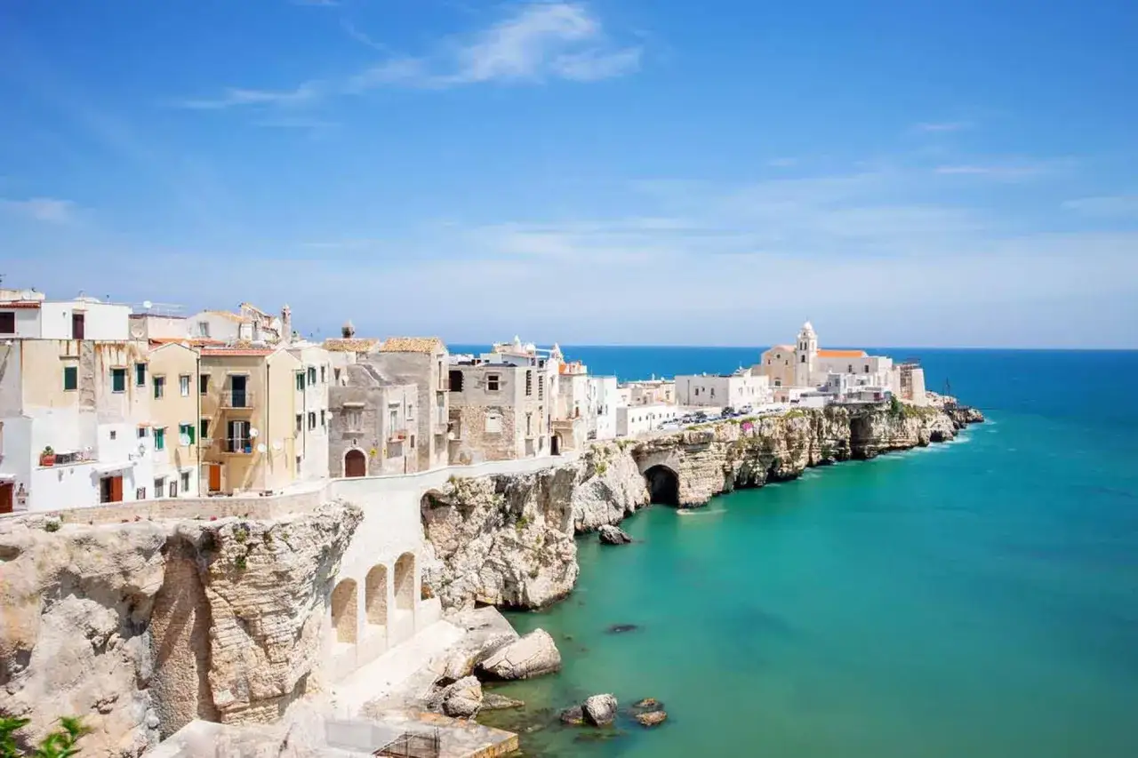 Vacker kuststad i Puglia, Italien, med vita hus som kl&auml;ttrar uppf&ouml;r klipporna mot det turkosbl&aring; havet.