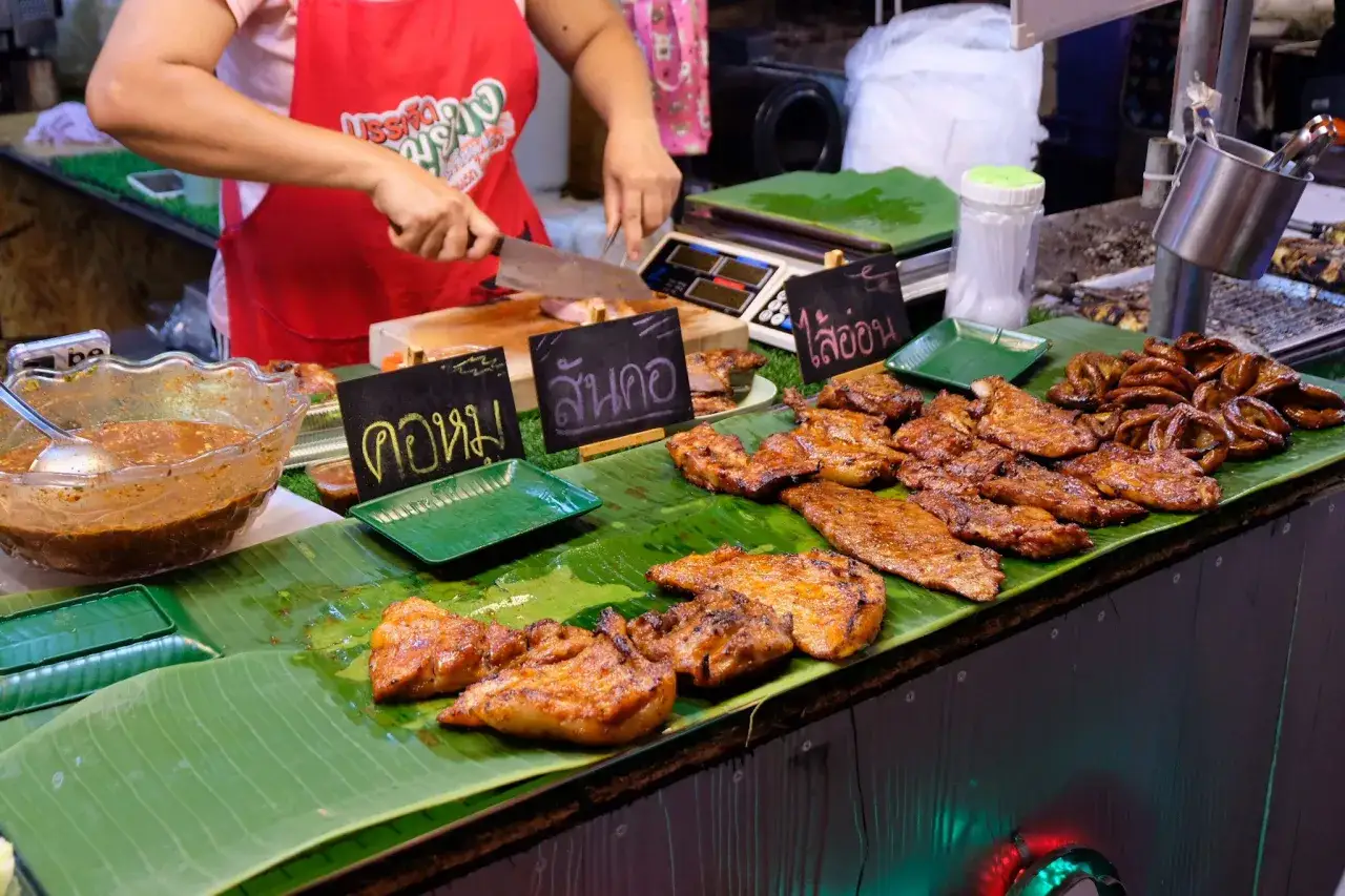 Grillad mat p&aring; bananblad, en del av den rika thailand matkultur. En s&auml;ljare sk&auml;r upp k&ouml;tt.