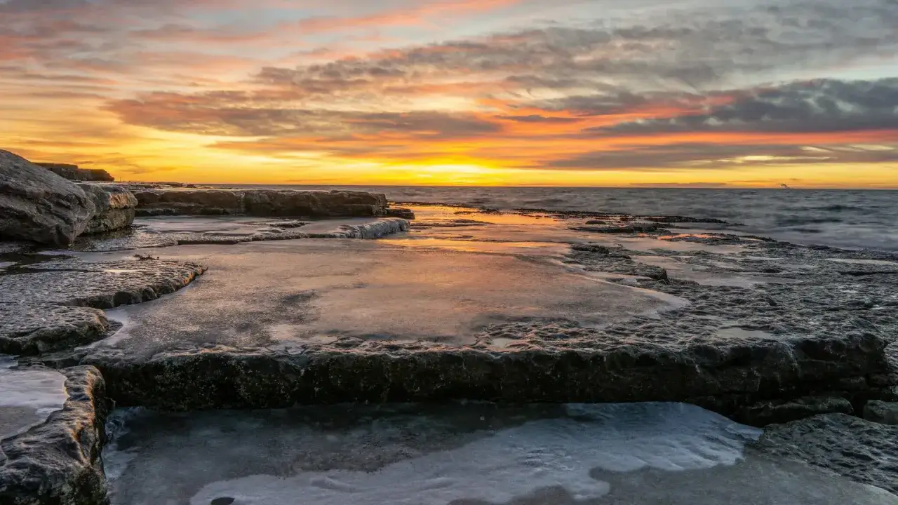 Isiga isiga solnedg&aring;ngar &ouml;ver ett isbelagt stenigt landskap vid havet.