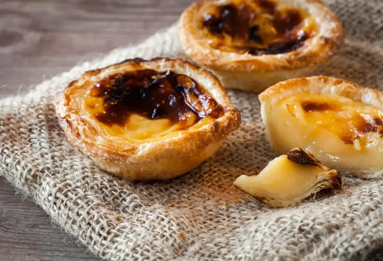 Tre kr&auml;miga portugisiska bakelser, ett uts&ouml;kt portugal mat, ligger p&aring; en jutduk.