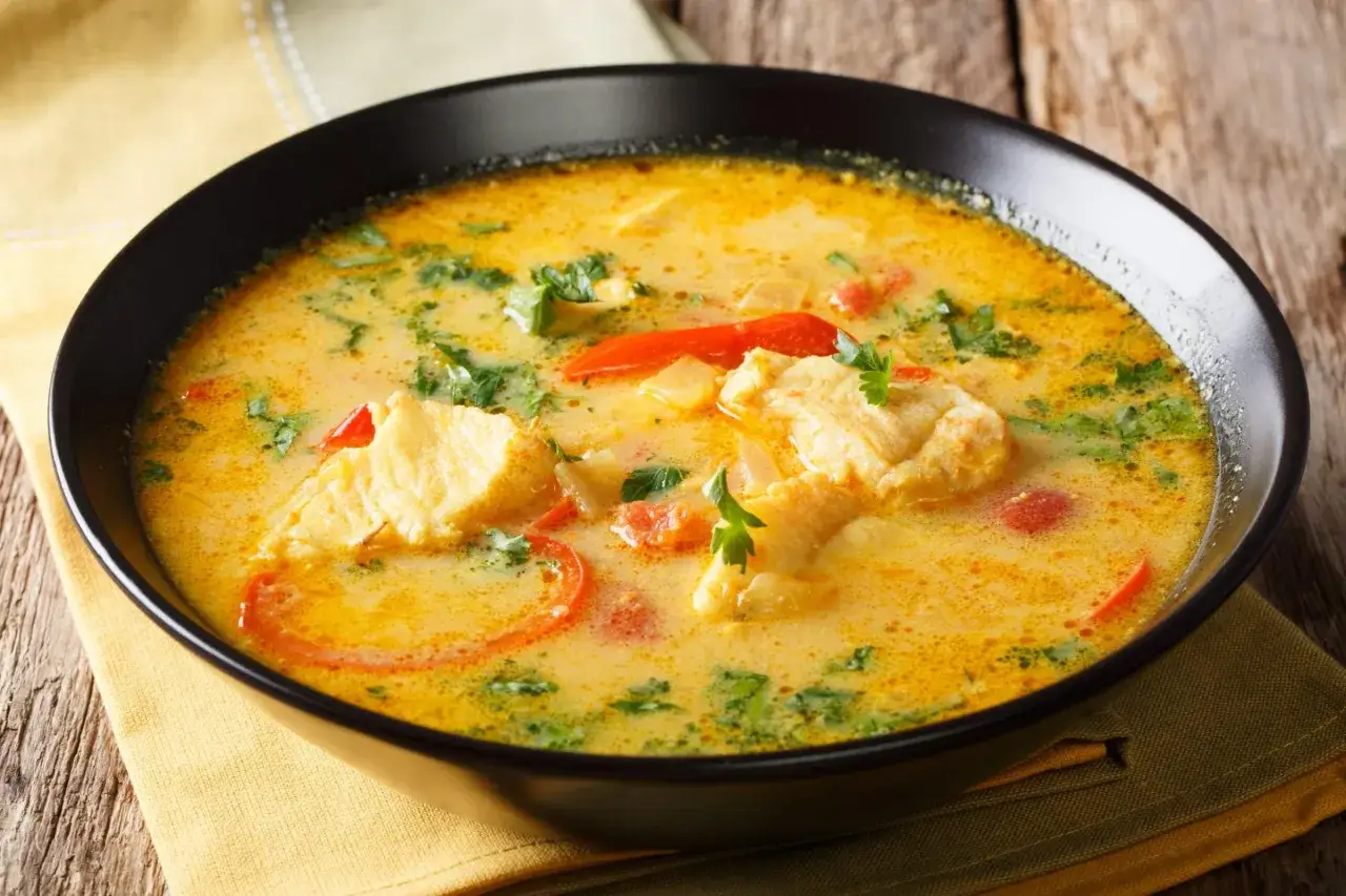 En n&auml;rbild av en kr&auml;mig portugisisk gryta med fiskbitar, tomater och f&auml;rska &ouml;rter i en svart sk&aring;l.