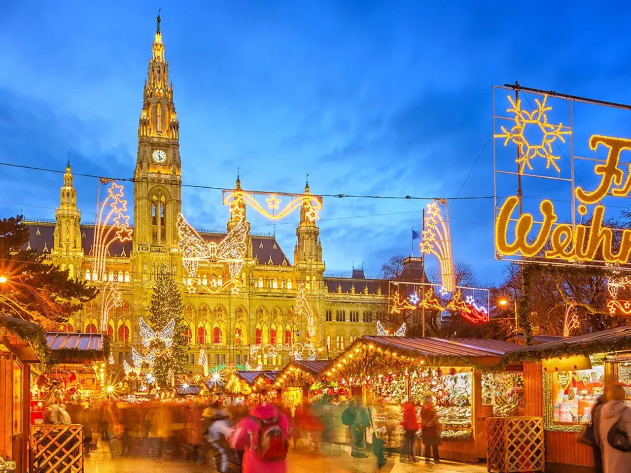 En magisk julmarknad i Wien med R&aring;dhuset i bakgrunden, upplyst av tusentals ljus. Folk strosar bland st&aring;nden.