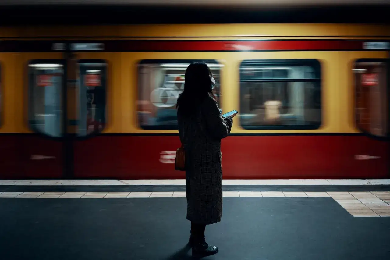 Kvinna med mobil p&aring; perrongen i Berlin, t&aring;get rusar f&ouml;rbi. En perfekt bild f&ouml;r din berlin reseguide.