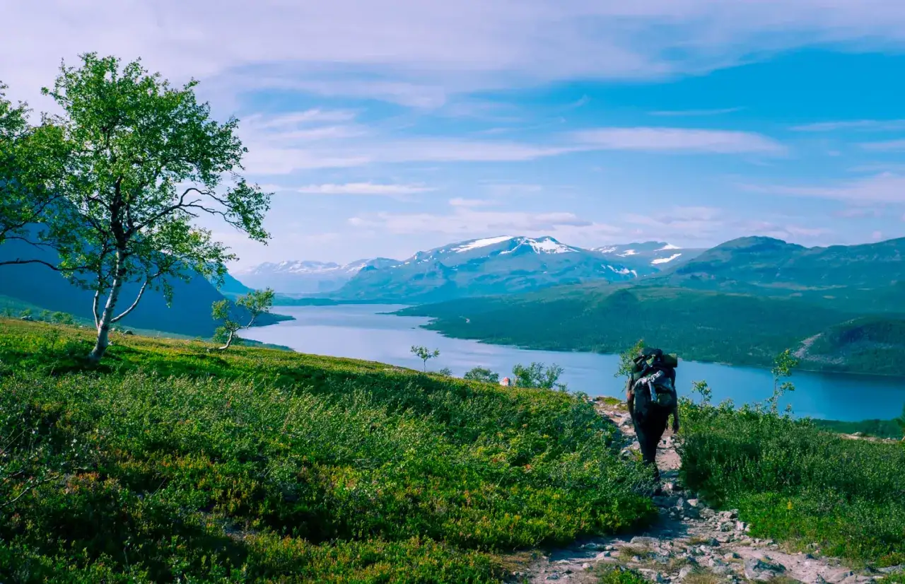 Vandrare med ryggs&auml;ck p&aring; en stenstig med utsikt &ouml;ver sj&ouml; och sn&ouml;kl&auml;dda berg. Fantastiska vandringsleder norrland.