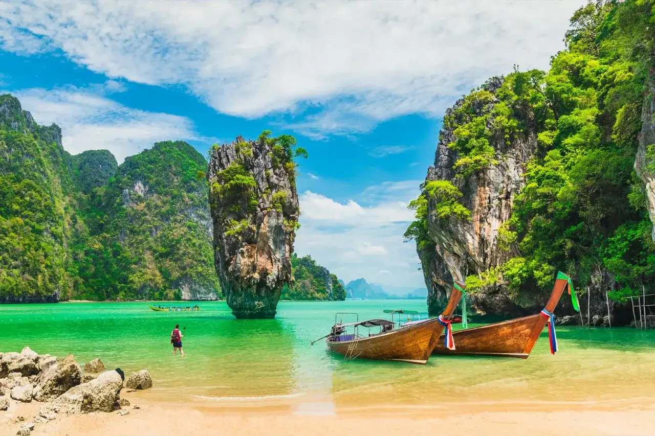 Tv&aring; tr&auml;b&aring;tar guppar i turkost vatten vid James Bond Island, omgivna av gr&ouml;na klippor och en sandstrand.