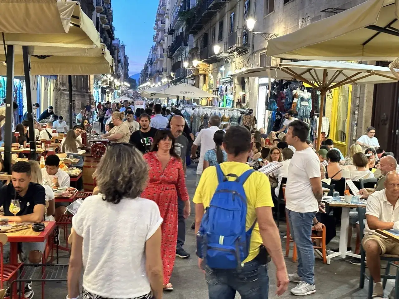En livlig kv&auml;llsgata i Palermo, Sicilien, med folk som &auml;ter utomhus och shoppar.