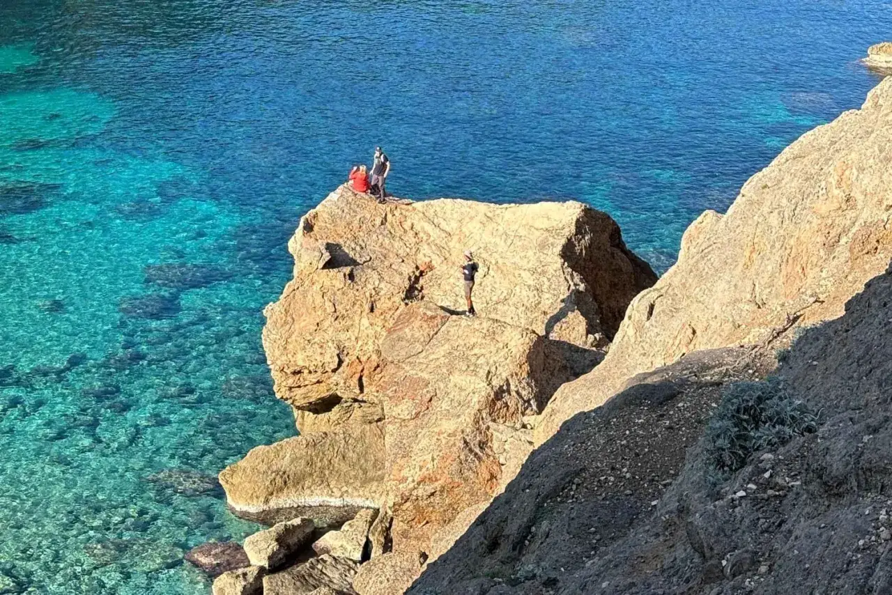 Vandra p&aring; Mallorca vid turkost vatten. Tre personer njuter av utsikten fr&aring;n en klippa.