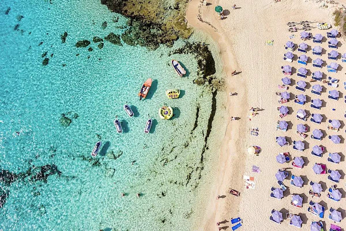 En strand p&aring; Cypern med turkost vatten, b&aring;tar och solstolar. Perfekt f&ouml;r att njuta av cypern temperatur &aring;ret runt.