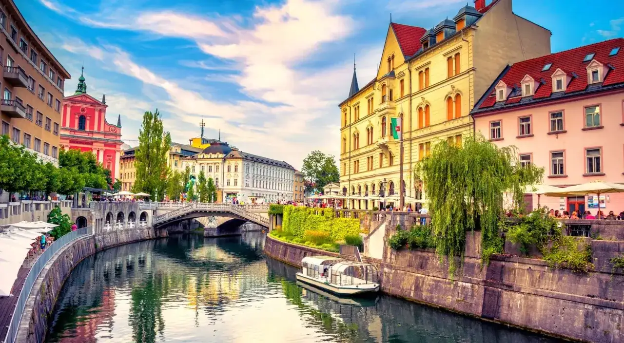 En vacker vy &ouml;ver Ljubljanas flod med en b&aring;t och en bro. En perfekt plats f&ouml;r en resa till Slovenien.