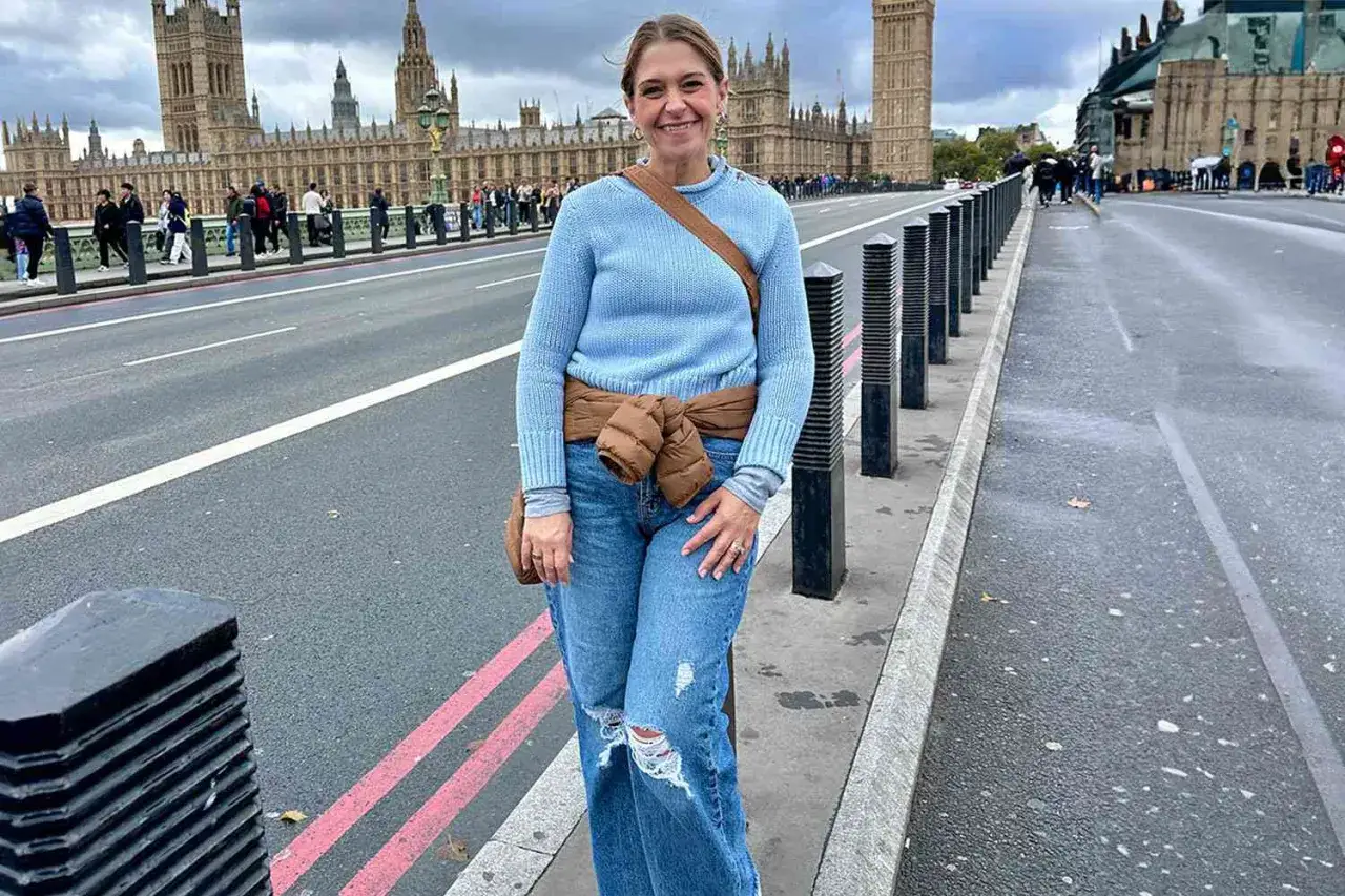 Kvinna i blå tröja och jeans poserar framför Houses of Parliament. Perfekt för en packlista London med bekväma kläder för stadsvandring.