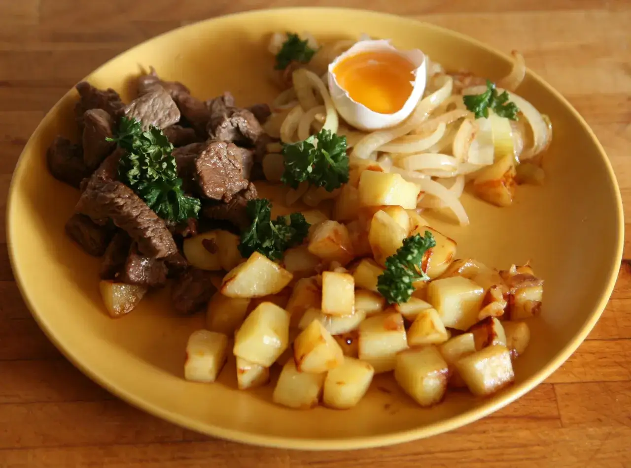 En tallrik med stekt k&ouml;tt, potatis och stekt l&ouml;k, toppad med ett r&aring;tt &auml;gg. En klassisk r&auml;tt fr&aring;n k&ouml;ket i Sverige.