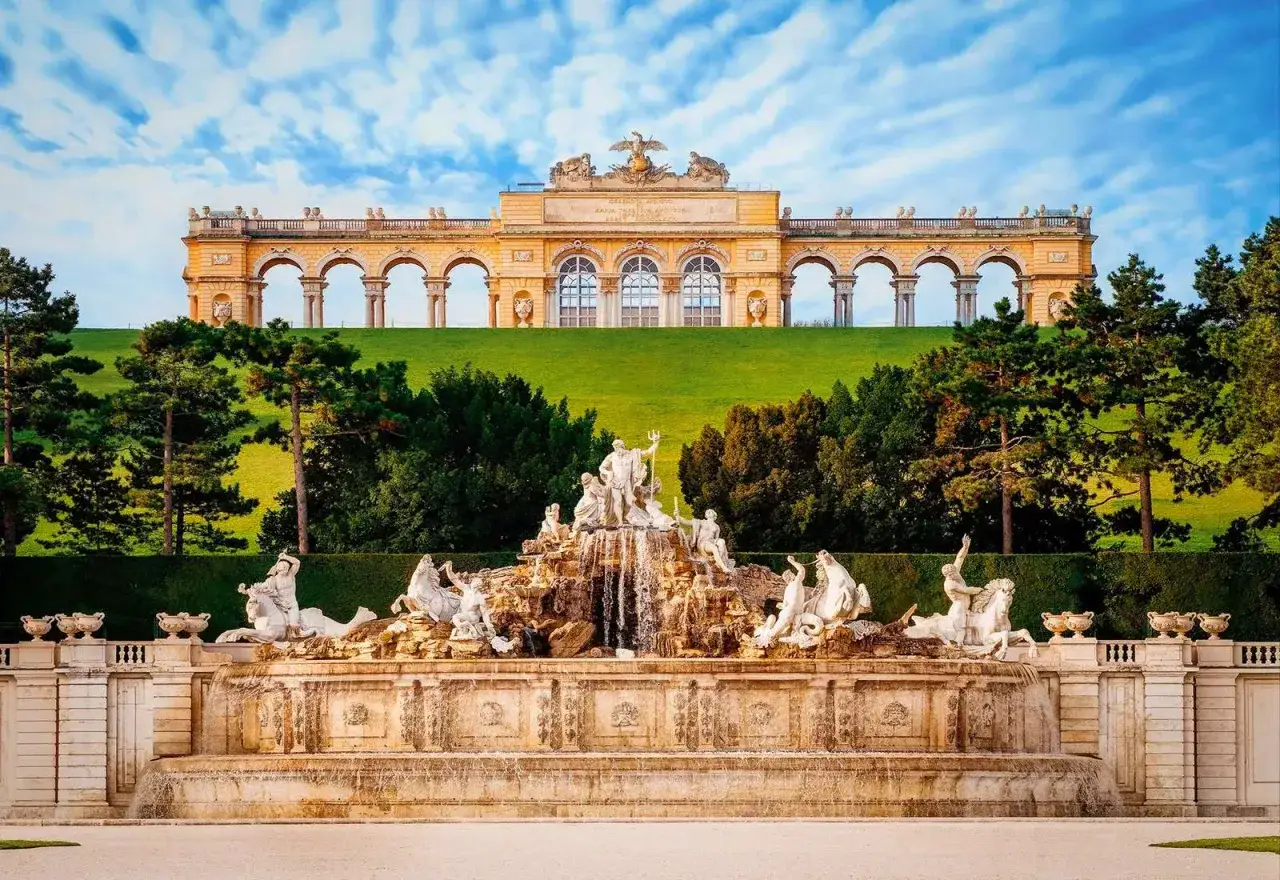 Sch&ouml;nbrunn-palatsets font&auml;n med statyer och en imponerande byggnad i bakgrunden. Ett m&aring;ste att se i Wien.