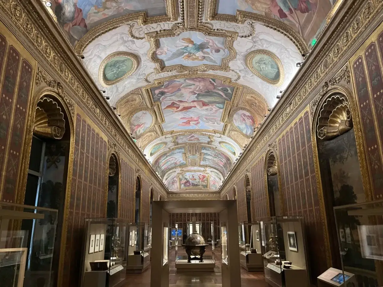 En magnifik sal i ett konstmuseum i Paris med ett rikt dekorerat tak med fresker och gyllene v&auml;ggar.