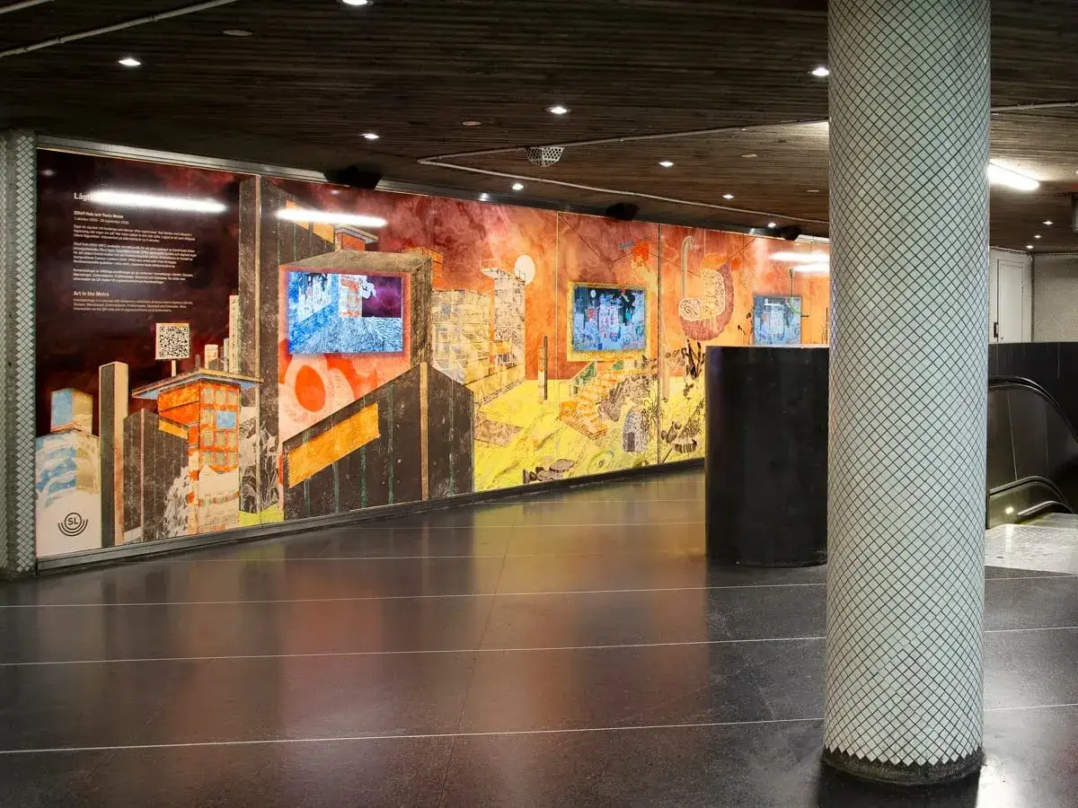 Stor v&auml;ggm&aring;lning med stadsmotiv och digitala sk&auml;rmar i en tunnelbanestation i Stockholm. Konstverket p&aring;minner om graffiti.