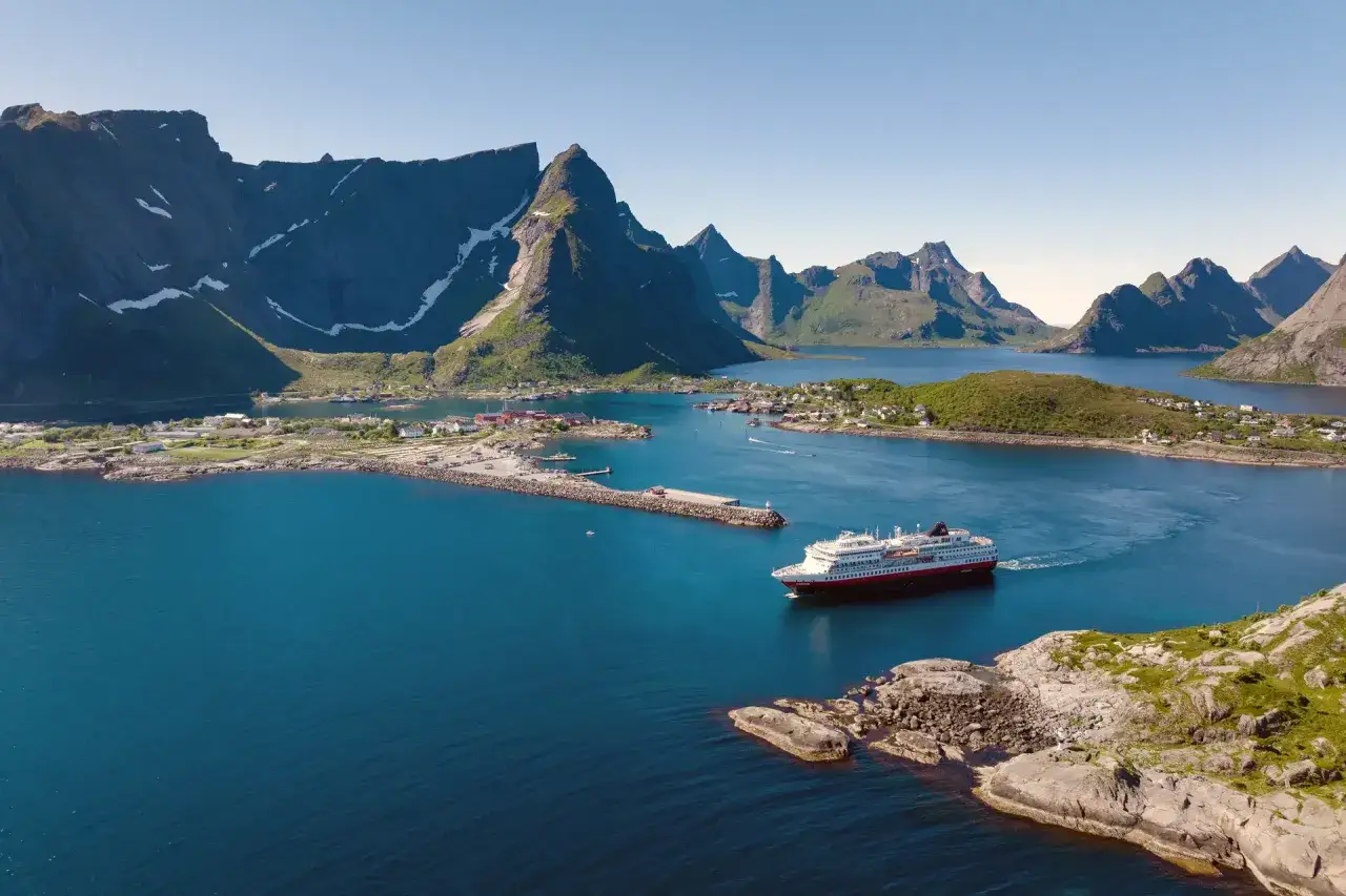 Fartyg passerar en pittoresk by vid foten av dramatiska berg. Fantastiska Lofoten tips f&ouml;r en of&ouml;rgl&ouml;mlig resa.