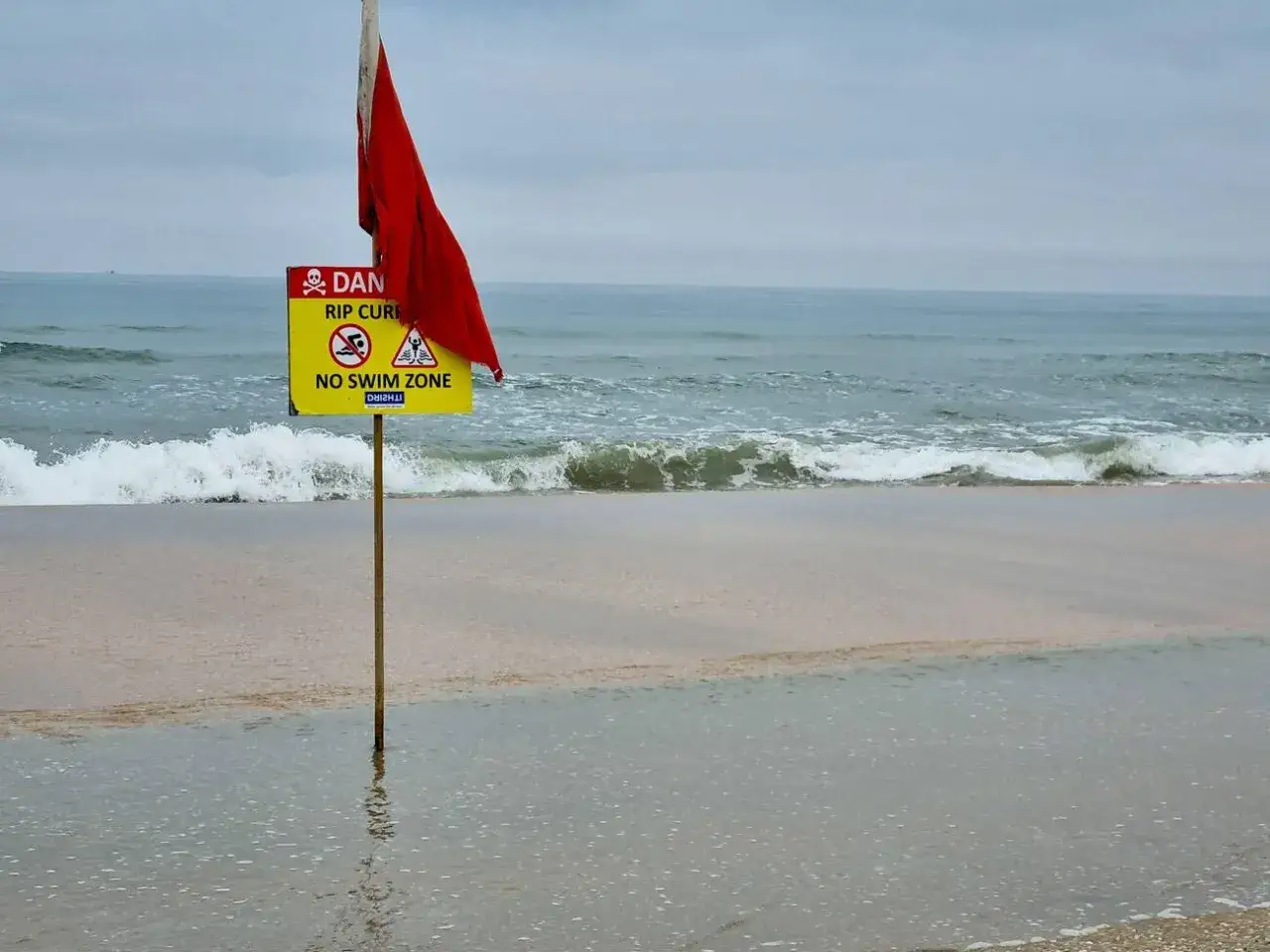 R&ouml;d flagga och skylt varnar f&ouml;r farliga str&ouml;mmar vid stranden. &Auml;ven om det ser goa ut, &auml;r det indien farligt att bada h&auml;r.