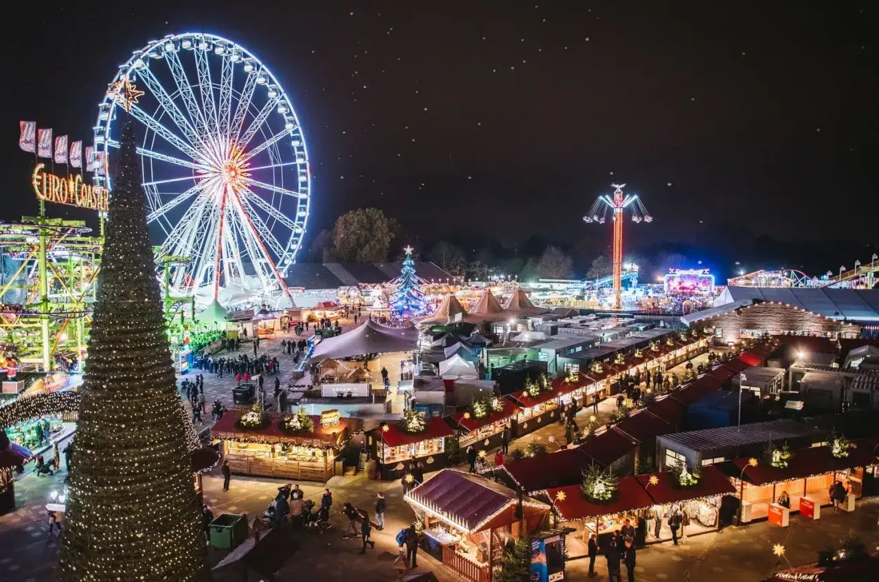 En livlig london julmarknad med ett stort pariserhjul, karuseller och julb&aring;s upplysta av tusentals ljus.