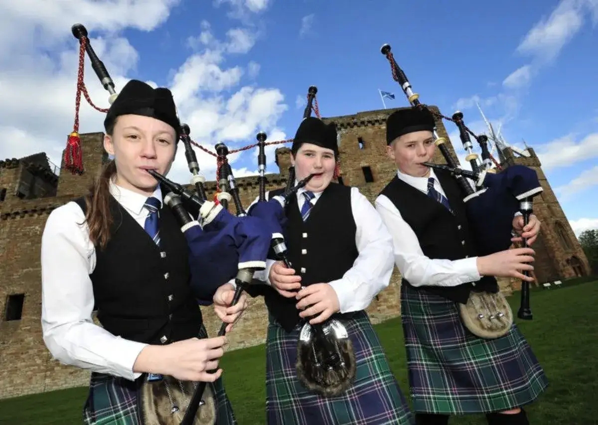 Tre unga s&auml;ckpipespelare i kilt firar skottlands nationaldag framf&ouml;r ett slott.