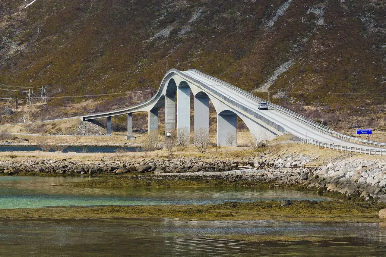 En bil k&ouml;r &ouml;ver en bro i Lofoten, en dr&ouml;mresa fr&aring;n Stockholm. Vackert landskap med berg och vatten.