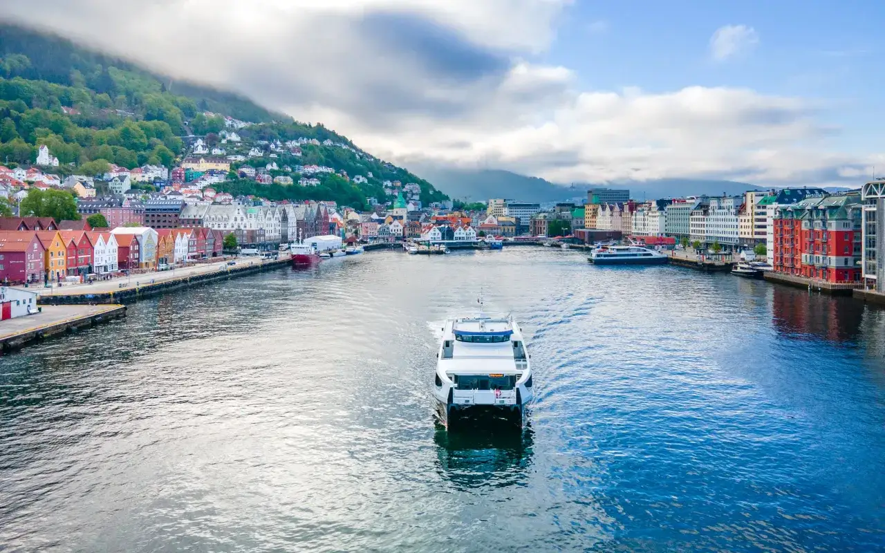 F&auml;rja p&aring; vattnet framf&ouml;r f&auml;rgglada hus och gr&ouml;na berg i Bergen.
