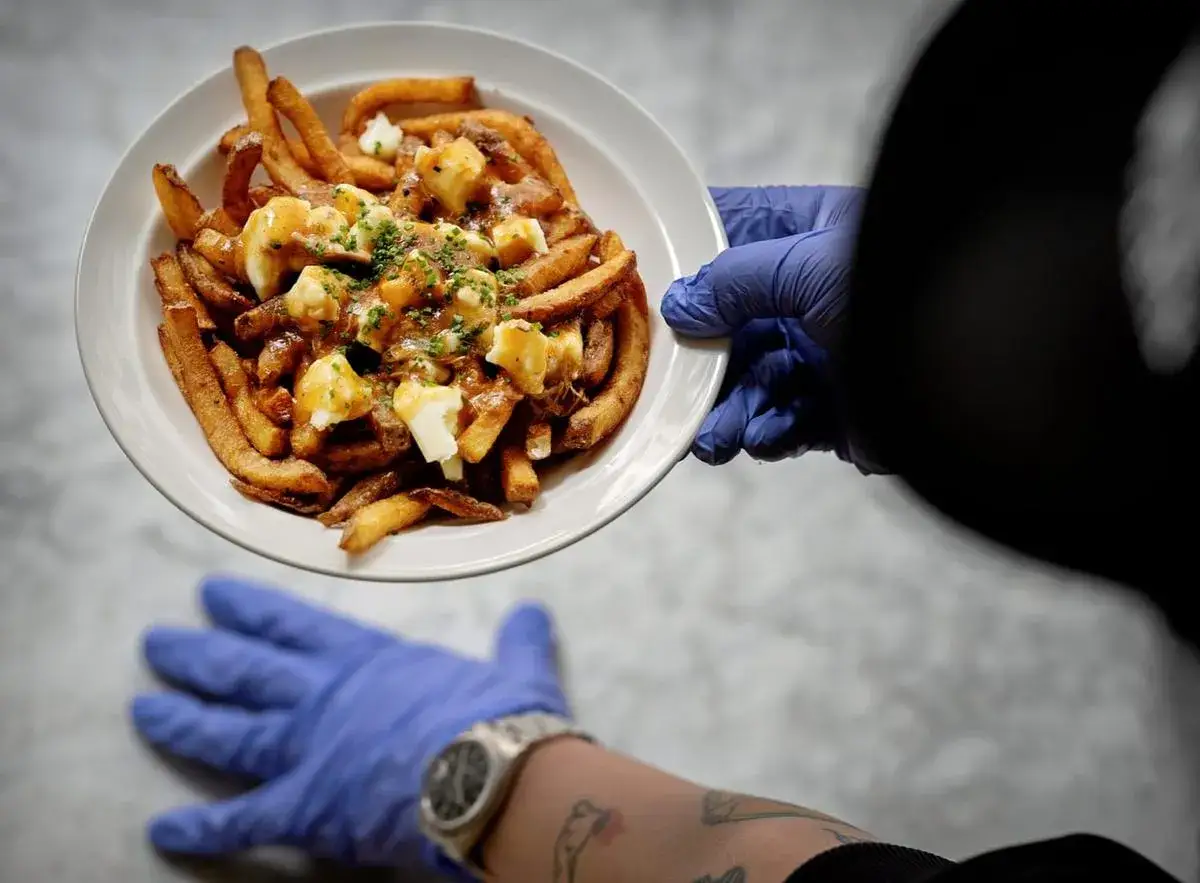 En tallrik med poutine, Kanadas nationalr&auml;tt, serveras. Pommes frites, ostbitar och s&aring;s toppas med persilja.