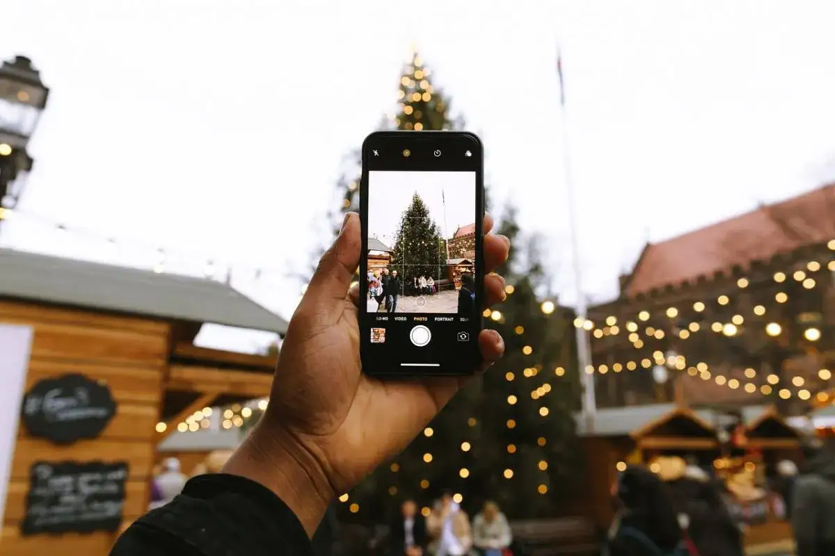 En hand h&aring;ller upp en mobiltelefon som fotograferar en julgran p&aring; en marknad i Alicante i december.