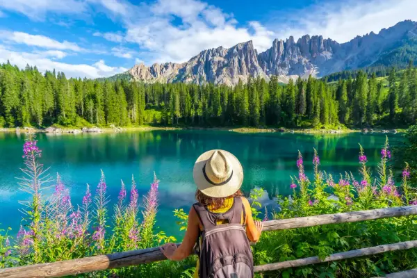 En kvinna med hatt och ryggsäck njuter av en vacker sommardag vid en turkos sjö i Dolomiterna.