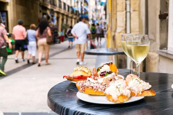 Tapas och vin på en uteservering i San Sebastián. Folk promenerar förbi på den livliga gatan.